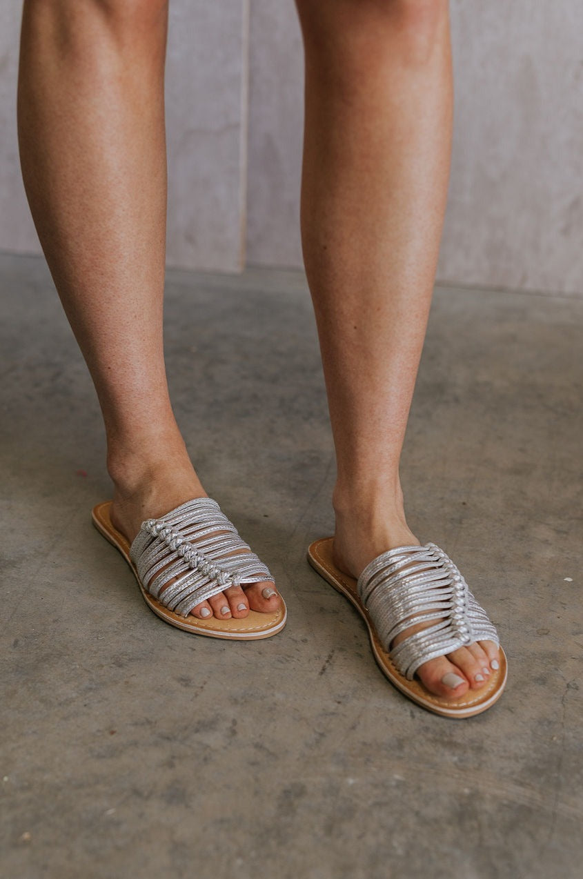 Front view of female model wearing the Baxter Sandal in Silver which features Silver Skinny Straps with Wooven Details,  Leather Upper, Padded Insole and Slip-On Style