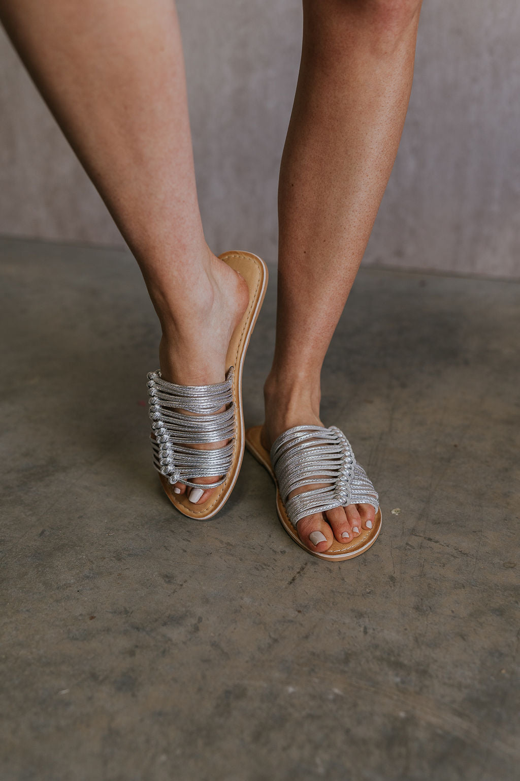 Front view of female model wearing the Baxter Sandal in Silver which features Silver Skinny Straps with Wooven Details, Leather Upper, Padded Insole and Slip-On Style