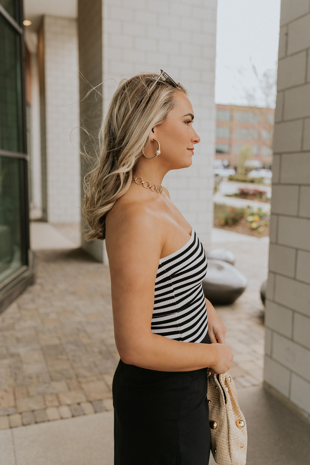 Upper body side view of female model wearing the Londyn White & Black Striped Tube Top that has horizontal white and black stripes and a straight strapless neckline. Worn with black skirt.