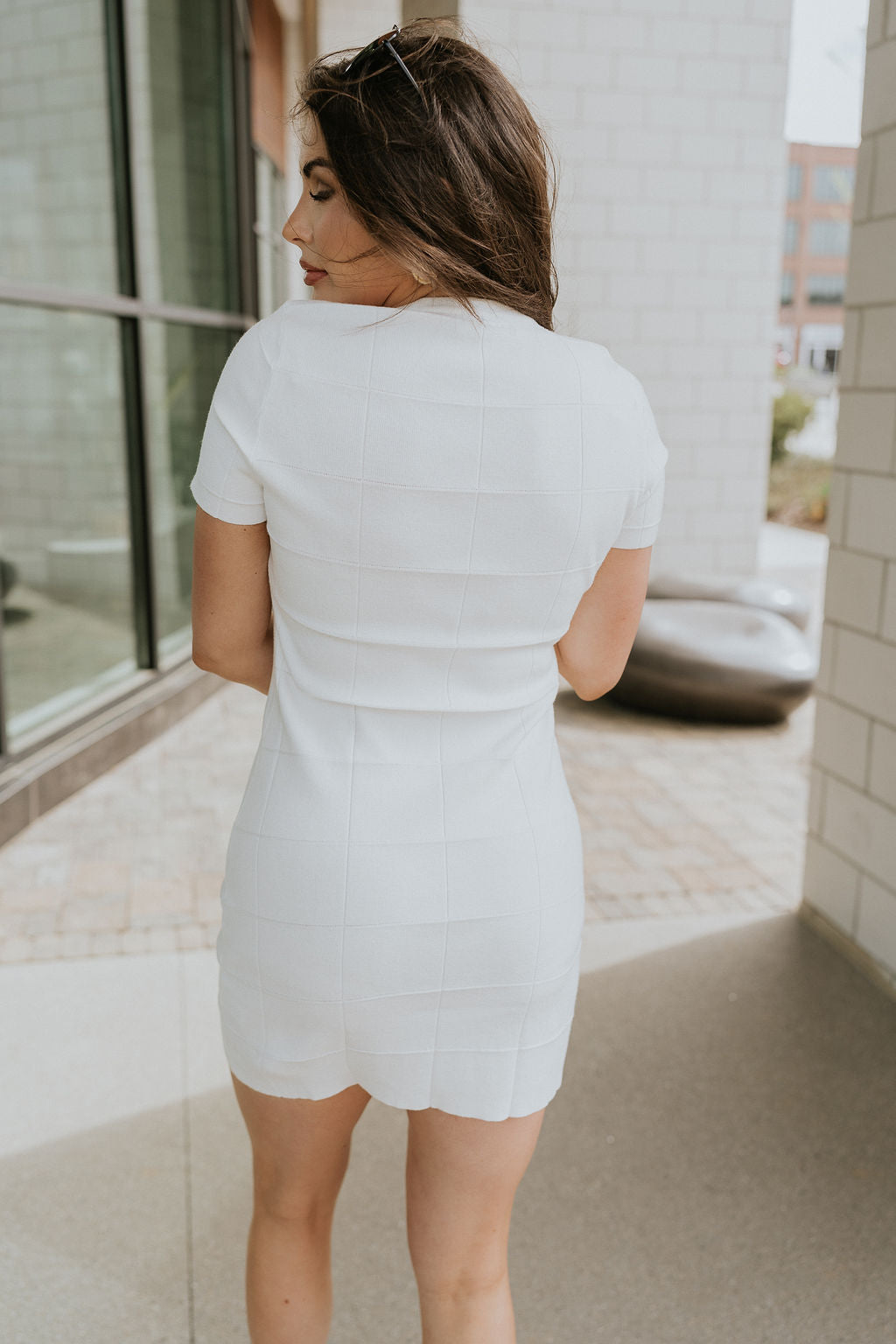 Back view of female model wearing the Sutton White Knit Checkered Mini Dress that has white knit fabric with a checkered texture, round neck, and short sleeves.