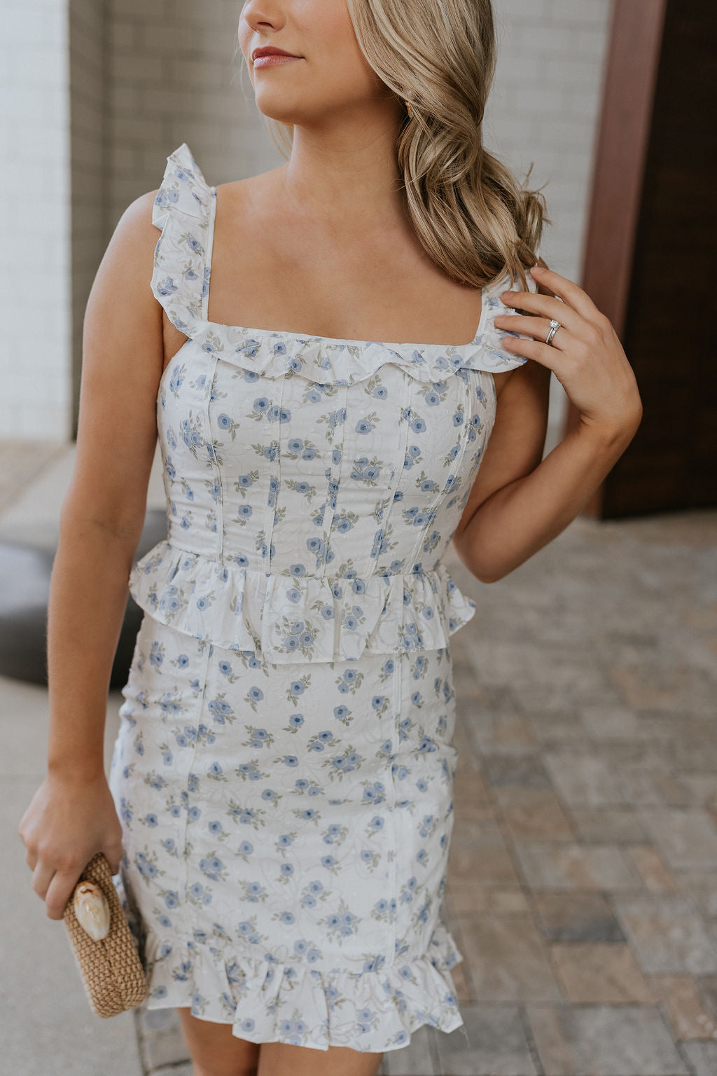 Close up view of female model wearing the Emerson White Blue Floral Ruffle Mini Dress which features White Lightweight Fabric, Blue Floral Print, Ruffle Hem Design, Square Neckline and sleeveless
