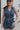 Front view of female model wearing the Georgia Belted Denim Romper in medium wash, that has a button up front, collar, and belted waist.