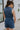 Back view of female model wearing the Georgia Belted Denim Romper in medium wash, that has a button up front, collar, and belted waist.
