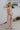Full body side view of female model wearing the Aleah Mauve Pink Sleeveless Jumpsuit which features Mauve Pink Lightweight Fabric, Wide Leg Pants, Upper Ruched Detail, Two Side Pockets, Scooped Neckline, Adjustable Straps and Open Back with Tie Closure and Zipper