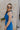 Side view of female model wearing the Juliette Blue Halter Tie Pleated Jumpsuit which features Blue Lightweight Fabric, Pleated Wide Pant Legs, Front Key Hole Design, Halter Neckline Tie Closure and Open Back