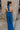 Full body back view of female model wearing the Juliette Blue Halter Tie Pleated Jumpsuit which features Blue Lightweight Fabric, Pleated Wide Pant Legs, Front Key Hole Design, Halter Neckline Tie Closure and Open Back