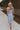 FUll body back view of female model wearing the Colette Light Blue Midi Dress which features Light Blue Lightweight Fabric, Midi Length, V-Neckline and Tie Straps