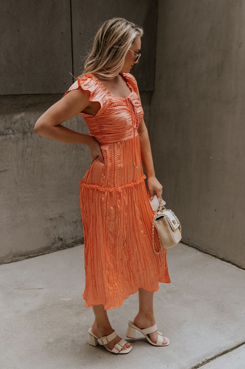 Side view of female model wearing the Maren Peach Key Hole Midi Dress which features Peach Crinkle Fabric, Midi Length, Peach Lining, Square Neckline with Key Hole Tie Closure, Ruffle Straps andTier Ruffle Skirt Detail