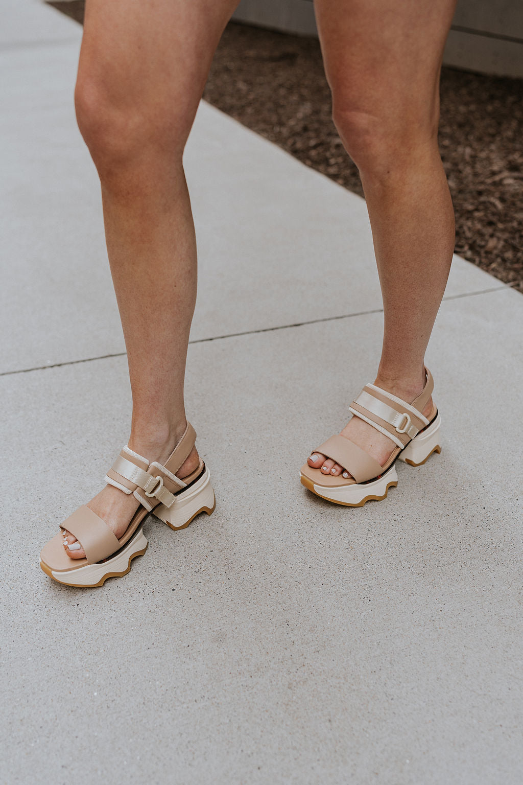 Side view of female model wearing the Kinetic Impact Slingback Heel in Honest Beige & Honest White which features Beige and Cream Leather Upper Fabric, Leather Strap, Adjustable Hook and Velcro Strap Closure, 1 1/2" Platform Sole, 2 1/12" Heel Height and Tortoise Sole Lining Details