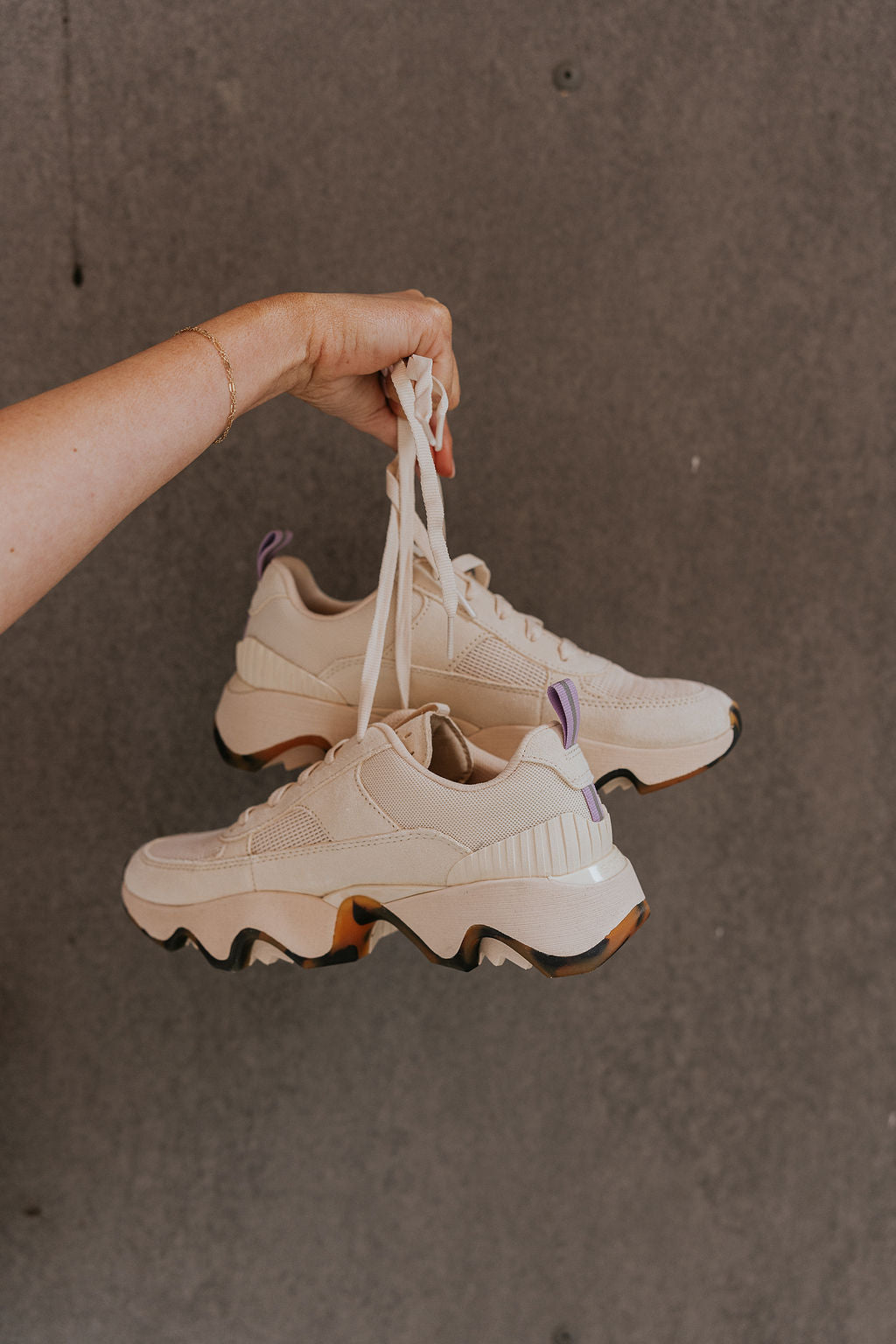 Front side view of female model holding the Kinetic Impact II Wonder Lace Sneaker in Honey White & Euphoric Lilac which features Light Beige Mesh Fabric & Suede/Leather Upper, Tortoise Detail Rubber Sole, Lace Up Details and Lavender Pull Tab .