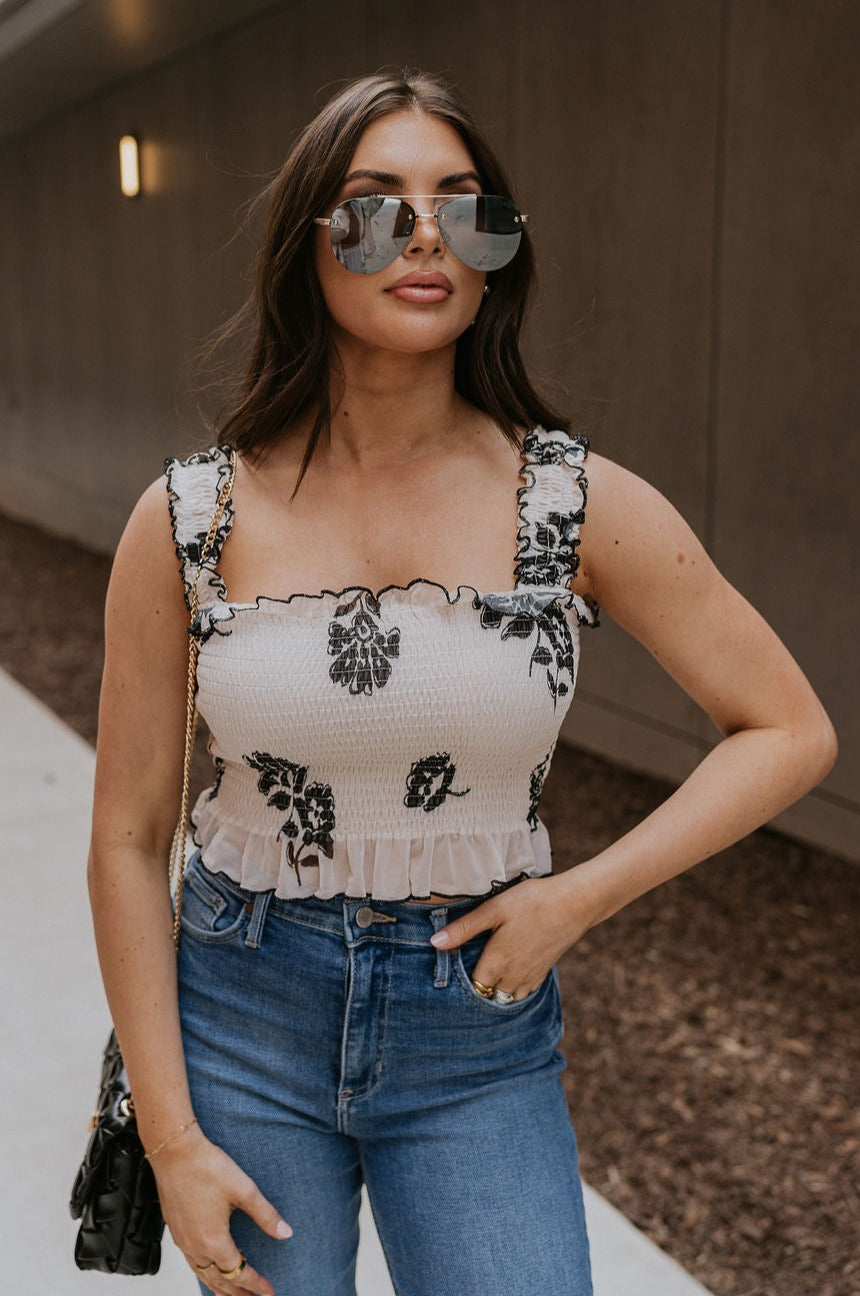 Front view of female model wearing the Elaina Black & Cream Floral Tank which features Black and Cream Floral Smocked Fabric, Cropped Waist, Lettuce Hem Details, Square Neckline and Thick Straps