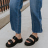 Side view of female model wearing the ONA Streetworks Slide Flat Sandal in Black & Chalk which features Black Light Foam Leather Upper, Two Straps, Slide-On Style, High-Traction Rubber Platform Sole and 2" Heel Height, 1 1/2" Platform Height