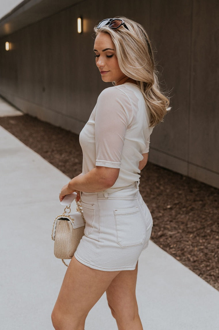 Side view of female model wearing the Lola Cream Sheer Short Sleeve Top which features Cream Sheer Fabric, Round Neckline, Cropped Waist and Short Sleeves