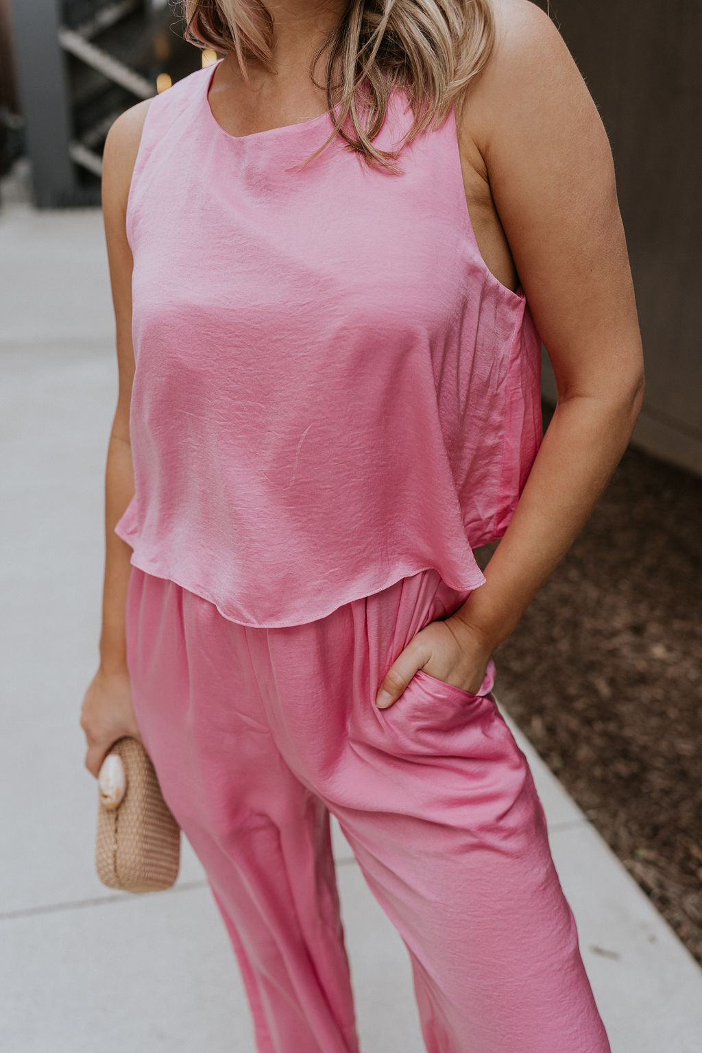 Close up view of female model wearing the Rowan Pink Sleeveless Jumpsuit which features Pink Satin Fabric, Wide Pant Legs, Round Neckline, Sleeveless and Back Key Hole with Button Closure