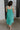 Full body back view of female model wearing the Vera Halter Cross Neckline Midi Dress in Green which features Lightweight Fabric, Lining, Midi Length, Side Ties Waistband, Halter Cross Neckline, Adjustable Straps and Sleeveless.