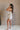 Side view of female model wearing the Elodie Beige Ruffle Tier Sleeveless Romper which features Beige Lightweight Fabric, Beige Lining, Ruffle Tier Details, Round Neckline, Sleeveless and Back Button Closure
