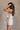 Side view of female model wearing the Elodie Beige Ruffle Tier Sleeveless Romper which features Beige Lightweight Fabric, Beige Lining, Ruffle Tier Details, Round Neckline, Sleeveless and Back Button Closure