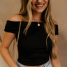 Close up front view of female model wearing the Isabella Off The Shoulder Cropped Tank in black, that features off the shoulder short sleeves, a straight neckline, and a cropped waist. 