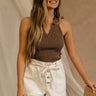 Front view of female model wearing the Fiona White Belted Denim Shorts, which have white denim, brown stitching, button fly, and pockets. Paired with brown tank top.
