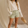 Full body view of female model wearing the Paige Sage Denim Shorts which features Light Sage Denim Fabric, Two Front Pockets,Two Back Pockets, Fray Hem and Belt Loops.