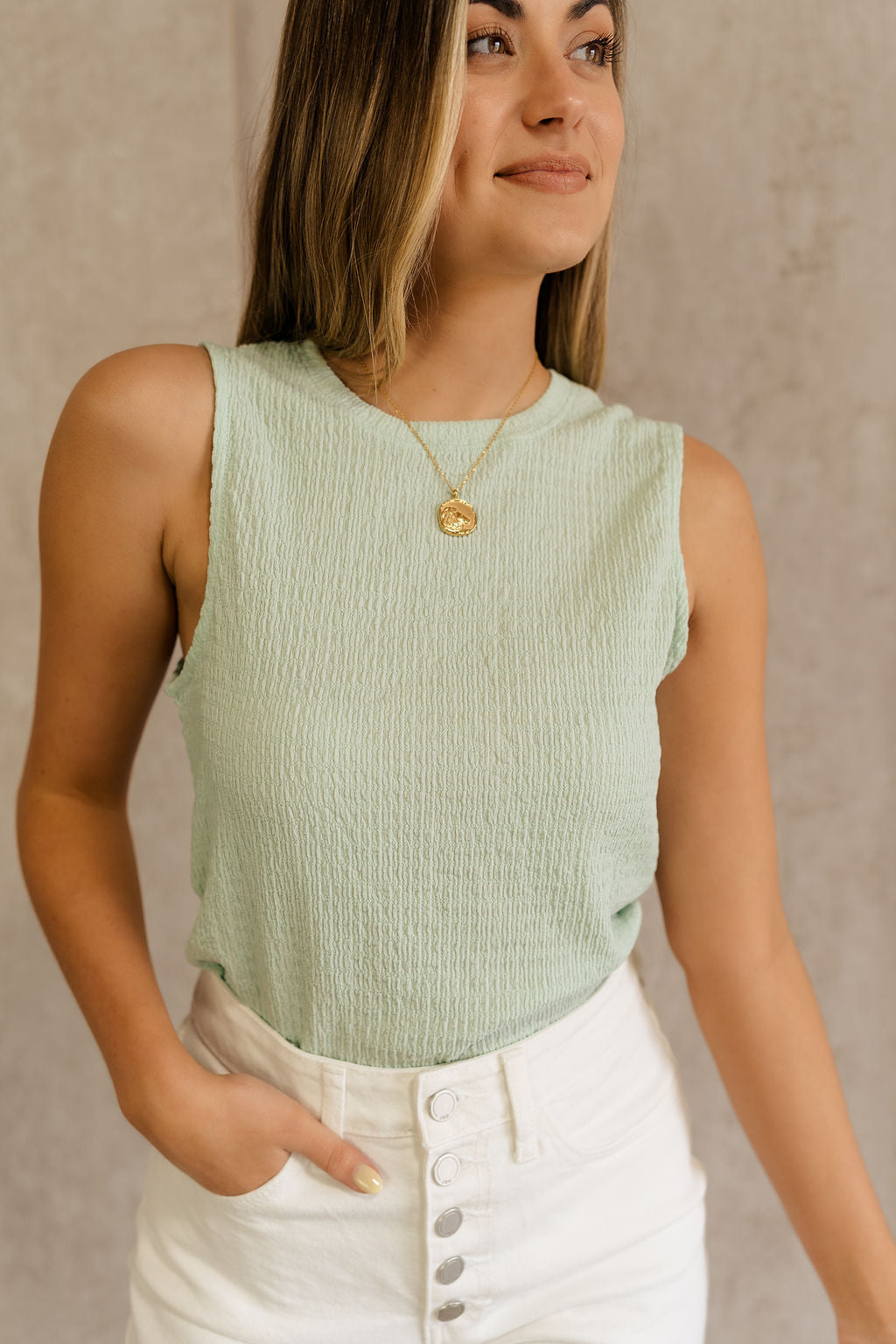 Front view of female model wearing the Kimber Mint Textured Tank that features mint green textured fabric, sleeveless body, and round neck. Tank is tucked into white shorts.