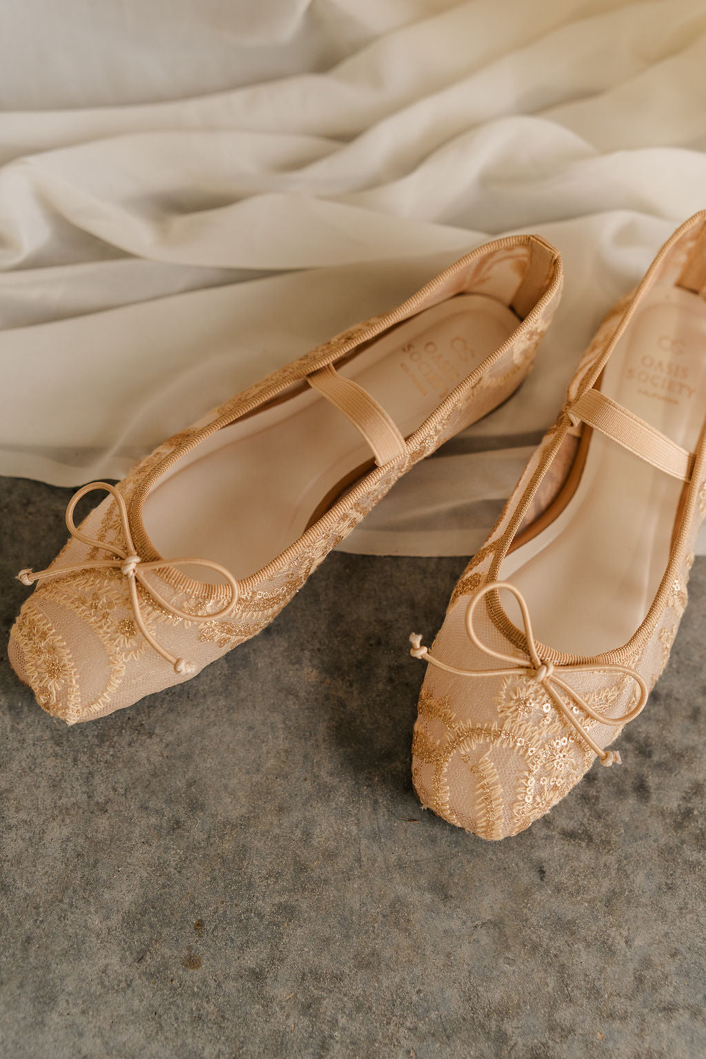 Top view of the Bisbee Ballet Flat in Gold that have beige mesh, ivory embroidery, gold sequins, a bow on front, and an elastic strap across the foot.