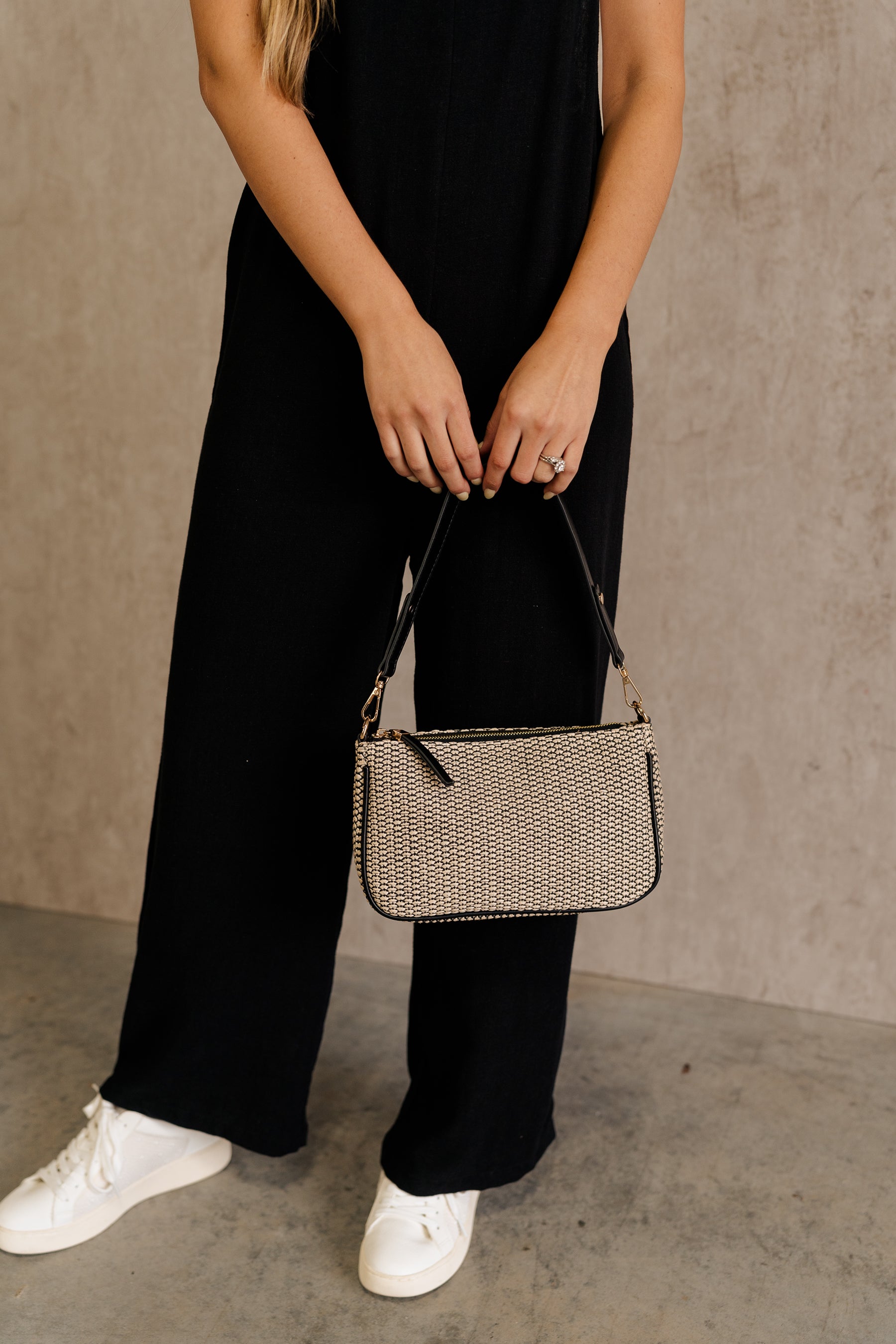 Front view of female model wearing the Haven Black &amp; Natural Woven Purse which features black and natural rattan fabric, black trim details, gold zipper closure and removable black strap.
