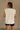 Back view of female model wearing the Ellie Off White Sleeveless Top which features white cotton fabric, ribbed hem, small side slits, round neckline and sleeveless