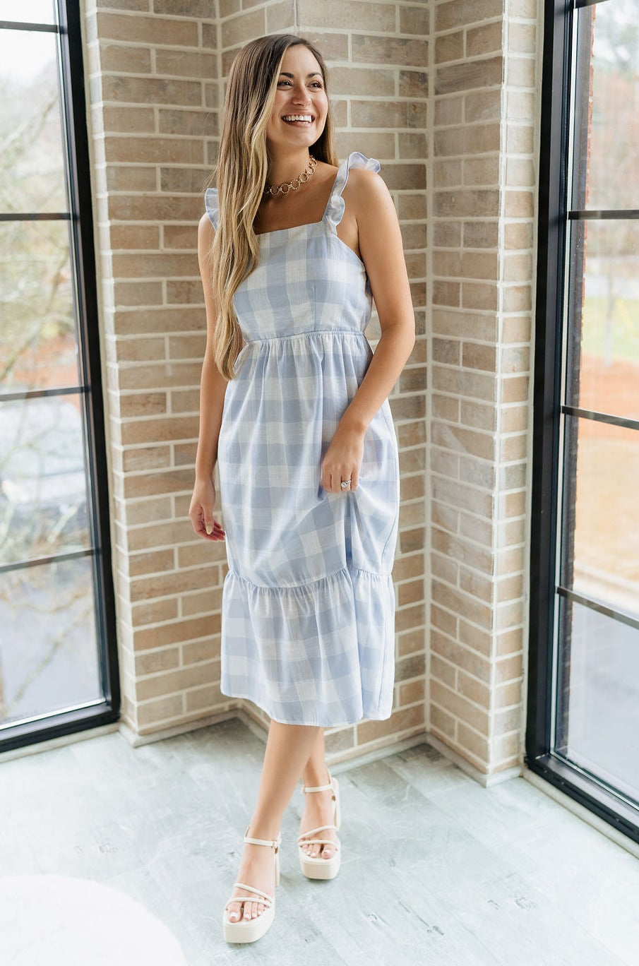 Full body view of female model wearing the Bonnie Light Blue and White Plaid Midi Dress which features Light Blue and White Plaid Design Midi Length, White Lining, Tiered Ruffle Hem, Square Neckline with Ruffle Straps and Sleeveless.