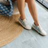 Side view of female model wearing the Helix Sneaker in Denim which features Light Wash Denim Fabric & White Faux Leather Fabric, Silver Metallic and Light Brown Details, Lace-Up Details and Round Toe.