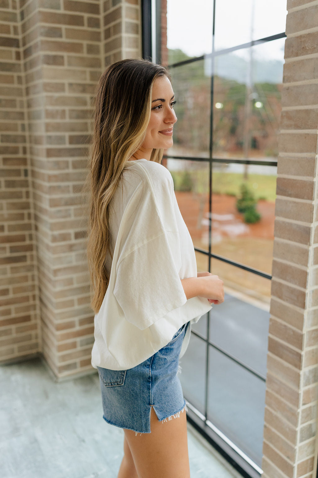 Side view of female model wearing the Melissa Off White Short Sleeve Top which features Off White Cotton Fabric, Round Neckline and Short Sleeves