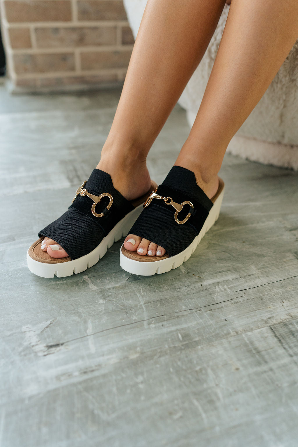 Front angle view of female model wearing the Venti Buckle Sandal in Black which features Fabric upper with gold buckle detail Slide on style for an easy on and off Memory foam footbed provides all day comfort 2.25 inch platform wedge Flexible rubber outsole.