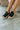 Front angle view of female model wearing the Venti Buckle Sandal in Black which features Fabric upper with gold buckle detail Slide on style for an easy on and off Memory foam footbed provides all day comfort 2.25 inch platform wedge Flexible rubber outsole.