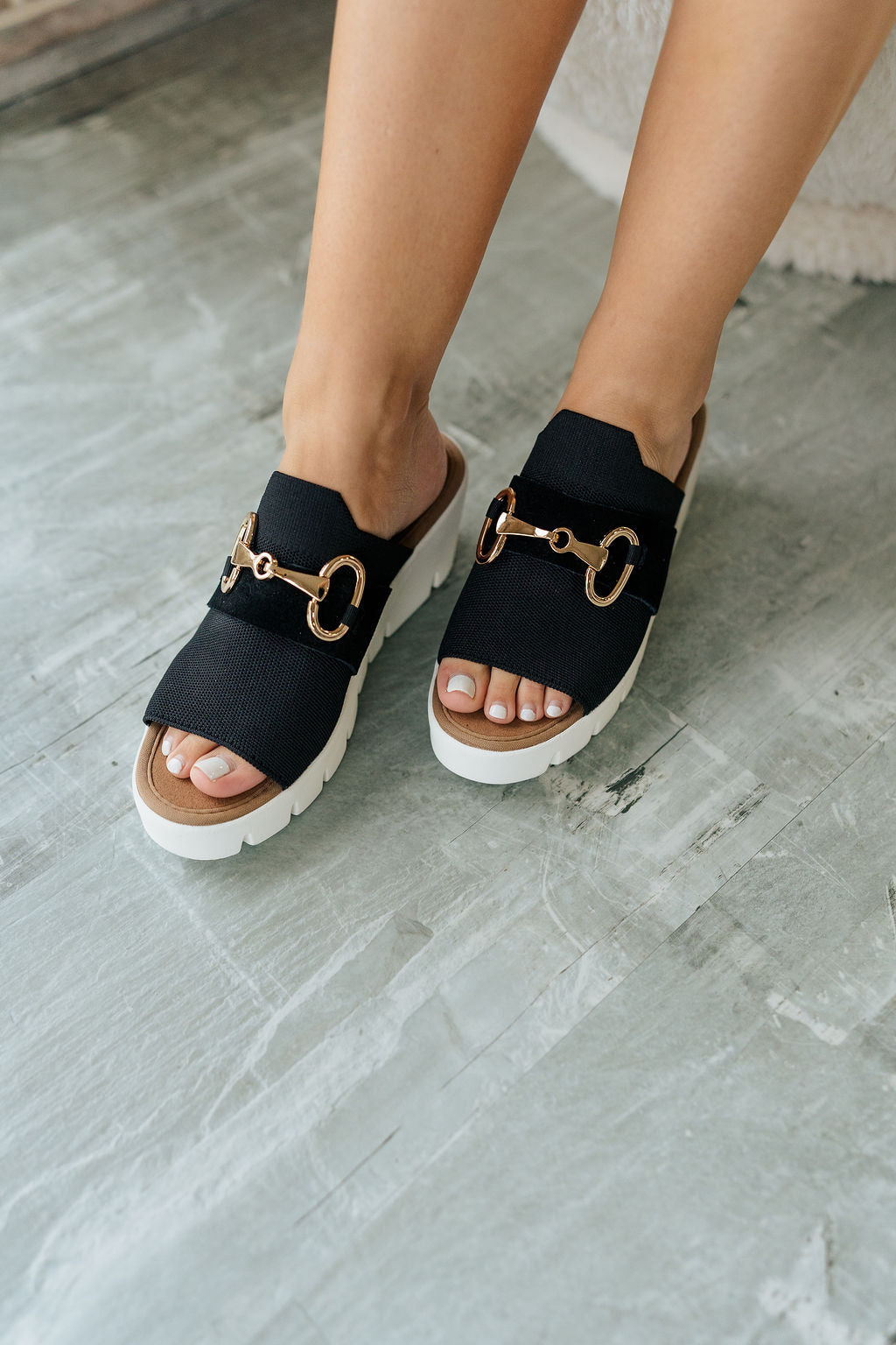 Close up view of female model wearing the Venti Buckle Sandal in Black which features Fabric upper with gold buckle detail Slide on style for an easy on and off Memory foam footbed provides all day comfort 2.25 inch platform wedge Flexible rubber outsole.