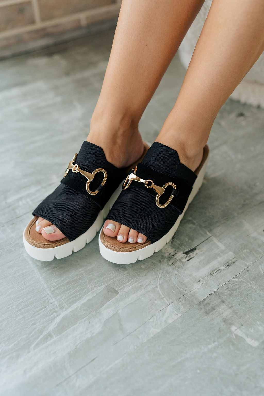Close up view of female model wearing the Venti Buckle Sandal in Black which features Fabric upper with gold buckle detail Slide on style for an easy on and off Memory foam footbed provides all day comfort 2.25 inch platform wedge Flexible rubber outsole.