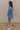 FUll body side view of model wearing the Marissa Blue and White Floral Short Sleeve Romper which features Blue Lightweight Fabric, White Floral Design, Blue Lining, Square Neckline, Short Puff Sleeves and Smocked Back.