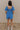 Full body back view of model wearing the Marissa Blue and White Floral Short Sleeve Romper which features Blue Lightweight Fabric, White Floral Design, Blue Lining, Square Neckline, Short Puff Sleeves and Smocked Back.