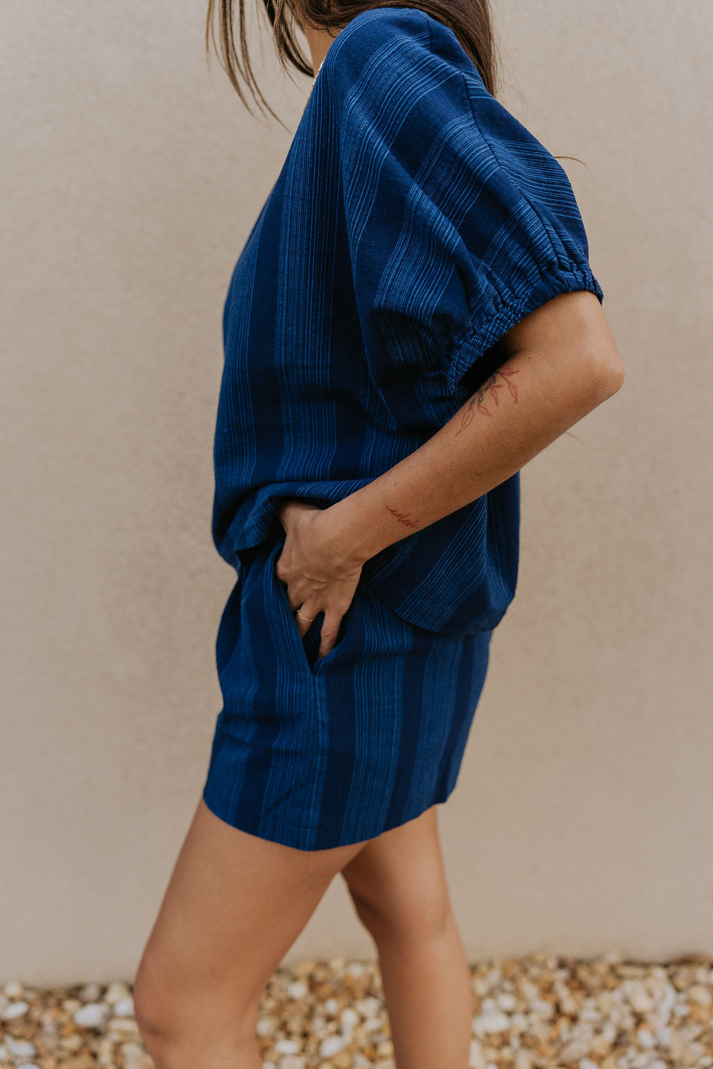 Side view of female model wearing the Julissa Navy Stripe Shorts which features Navy Blue with Light Blue Stripe Design, Elastic Waistband, Two Front Pockets and Two Back Pockets.