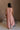 Full body back view of female model wearing the Brooklyn Sleeveless Wide Leg Jumpsuit in salmon pink which features Wide Pant Legs, Two Front Pockets, Lined Pant Legs, Round Neckline and Sleeveless.