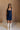Full body view of female model wearing the Stella Dark Denim Wash Sleeveless Mini Dress which features features Dark Denim Wash Fabric, Front Zip-Up Closure, Square Neckline and Sleeveless.