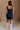 Full body back view of female model wearing the Stella Dark Denim Wash Sleeveless Mini Dress which features features Dark Denim Wash Fabric, Front Zip-Up Closure, Square Neckline and Sleeveless.