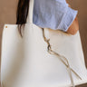 Close up side view of model wearing the Jolene Ivory Faux-Leather Tote Bag on her shoulder; this is a faux leather ivory tote bag with shoulder straps and a gold hook closure on front.