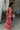 Full body side view of model wearing the Roselyn Pink & Red Floral Maxi Dress that has light pink fabric with dark pink and red floral pattern, a cowl neckline, and spaghetti straps that cross in the back.