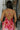 Upper back view of model wearing the Roselyn Pink & Red Floral Maxi Dress that has light pink fabric with dark pink and red floral pattern, a cowl neckline, and spaghetti straps that cross in the back.