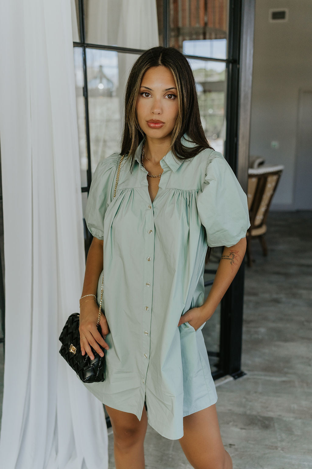 front view of model wearing the Marianna Sage Short Sleeve Dress that has sage green fabric, a button-up front, collar, and short puff sleeves.
