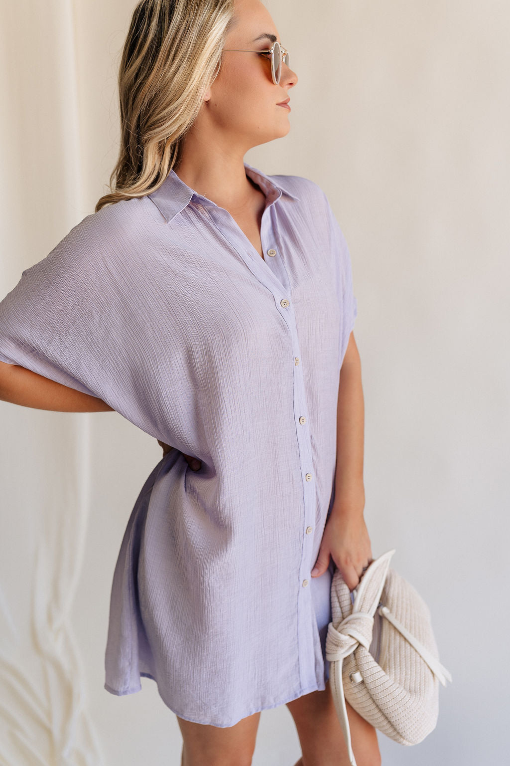 Side view of female model wearing the Luna Lavender Button-Up Short Sleeve Mini Dress which features Lavender Lightweight Fabric, Button-Up Front Closure, Collared Neckline and Short Sleeves