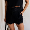 Front view of female model wearing the Stella Black Floral Trim Shorts which features Black Knit Fabric, Scalloped Hem with Open Details,  Monochrome Floral Print, Front Zipper with Button Closure, Two Front Pockets and Belt Loops