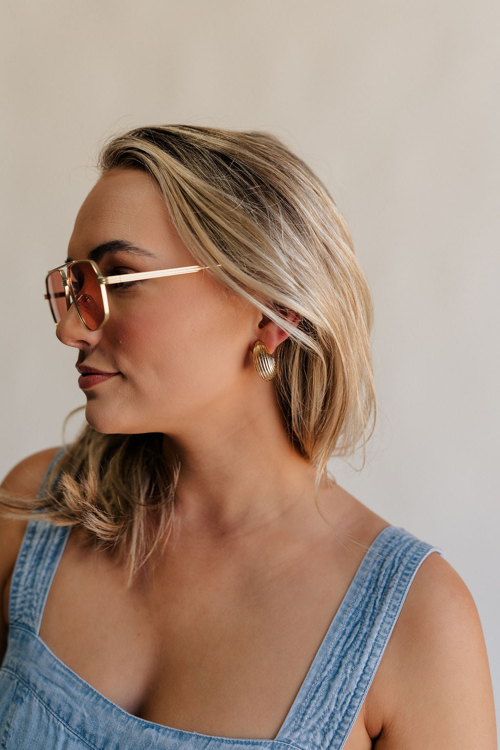 Side view of female model wearing the Alexis Gold Ribbed Scooped Stud Earring which features gold ribbed scoop shaped studs with back clasp closure