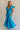 Full body view of female model wearing the Gianna Ruffle Short Sleeve Tiered Maxi Dress in Blue which features Lightweight Fabric, Tiered Body, Midi Length, Pockets on each side, V-Neckline with a Tie Detail and Ruffle Short Sleeves. the dress is available in pink, aqua blue and white.