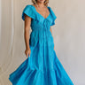 Full body view of female model wearing the Gianna Ruffle Short Sleeve Tiered Maxi Dress in Blue which features Lightweight Fabric, Tiered Body, Midi Length, Pockets on each side, V-Neckline with a Tie Detail and Ruffle Short Sleeves. the dress is available in pink, aqua blue and white.